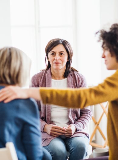 Serious men and women sitting in a circle during group therapy, supporting each other.