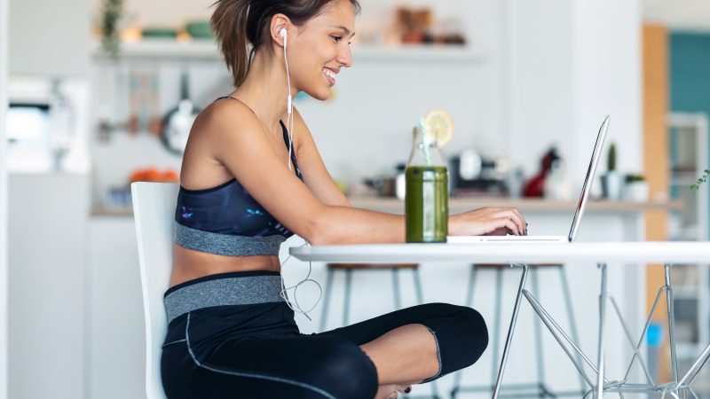 Shot of sporty young woman working with her laptop after session of exercises in the kitchen at home.