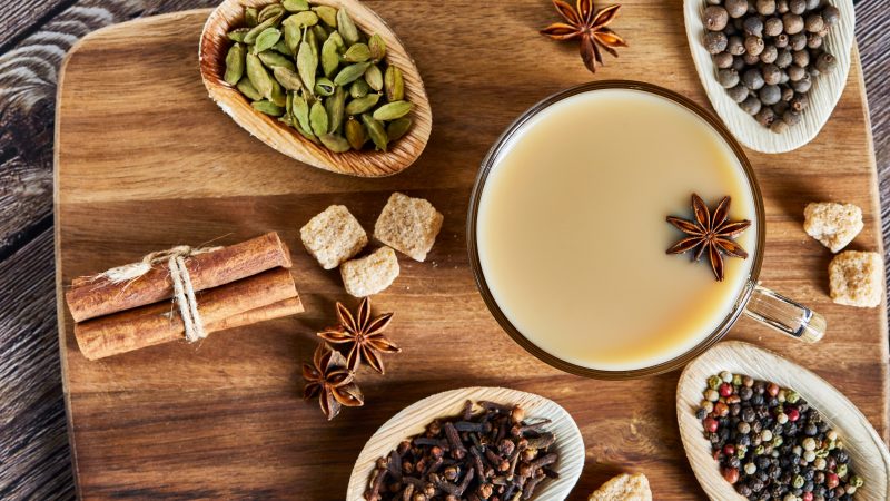 Traditional Indian drink - masala tea with spices. Cinnamon, cardamom, anise, sugar, cloves, pepper on a dark wooden background. Copy space. Flat lay.