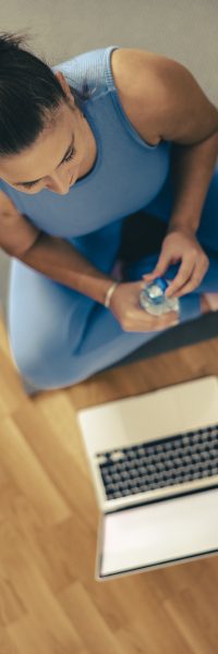 Young woman is holding water bottle and resting after online training at home in the morning.