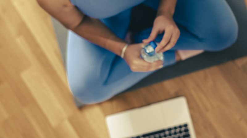 Young woman is holding water bottle and resting after online training at home in the morning.