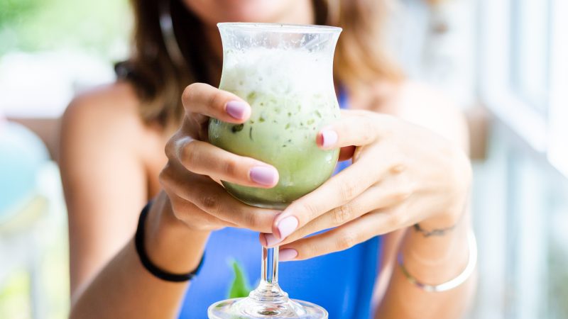 woman holds japanese matcha green tea with ice in glass in cafe