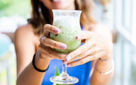 woman holds japanese matcha green tea with ice in glass in cafe